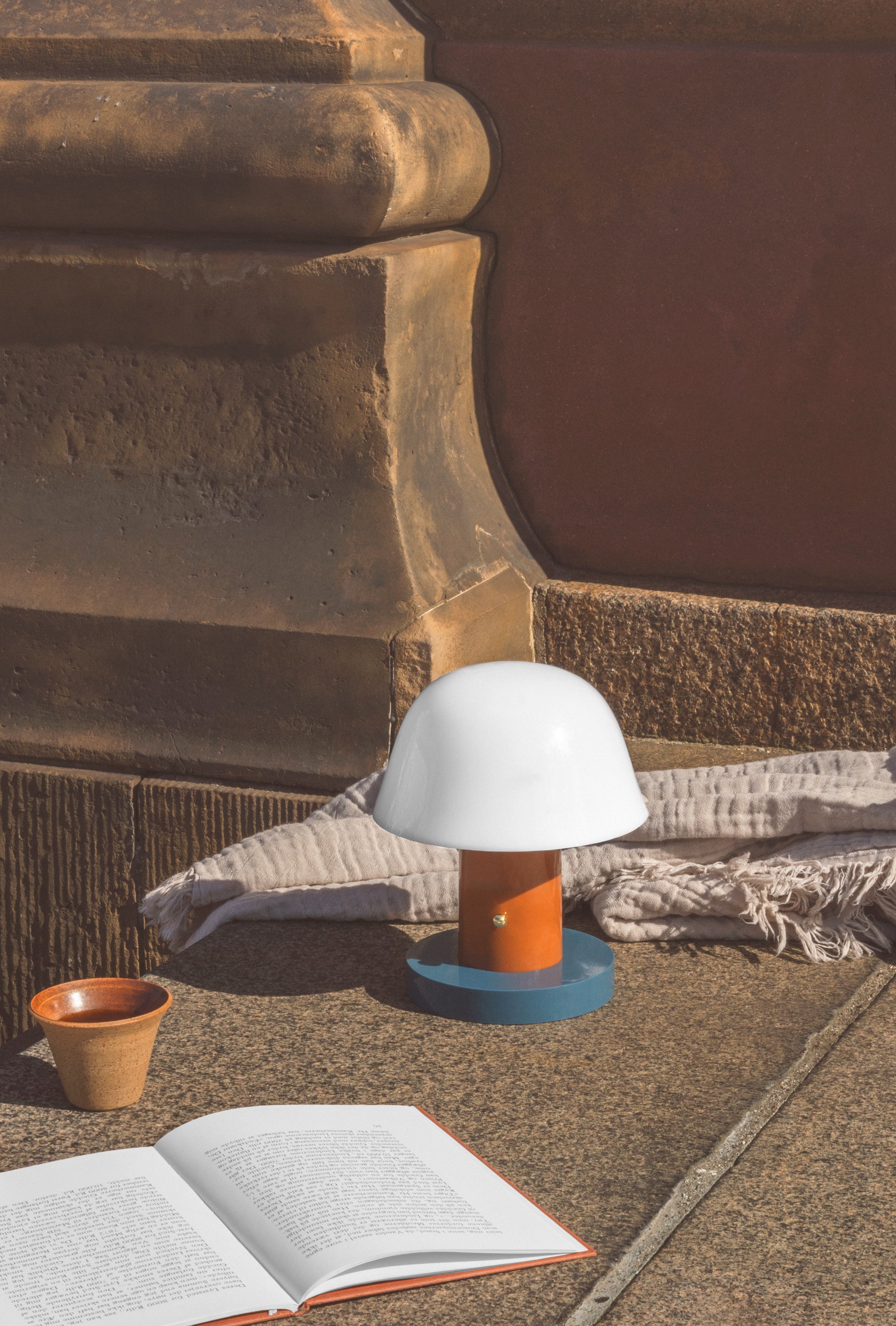 Prenosná lampa SETAGO JH27 s krémovým tienidlo a oranžovo-modrým podstavcom.