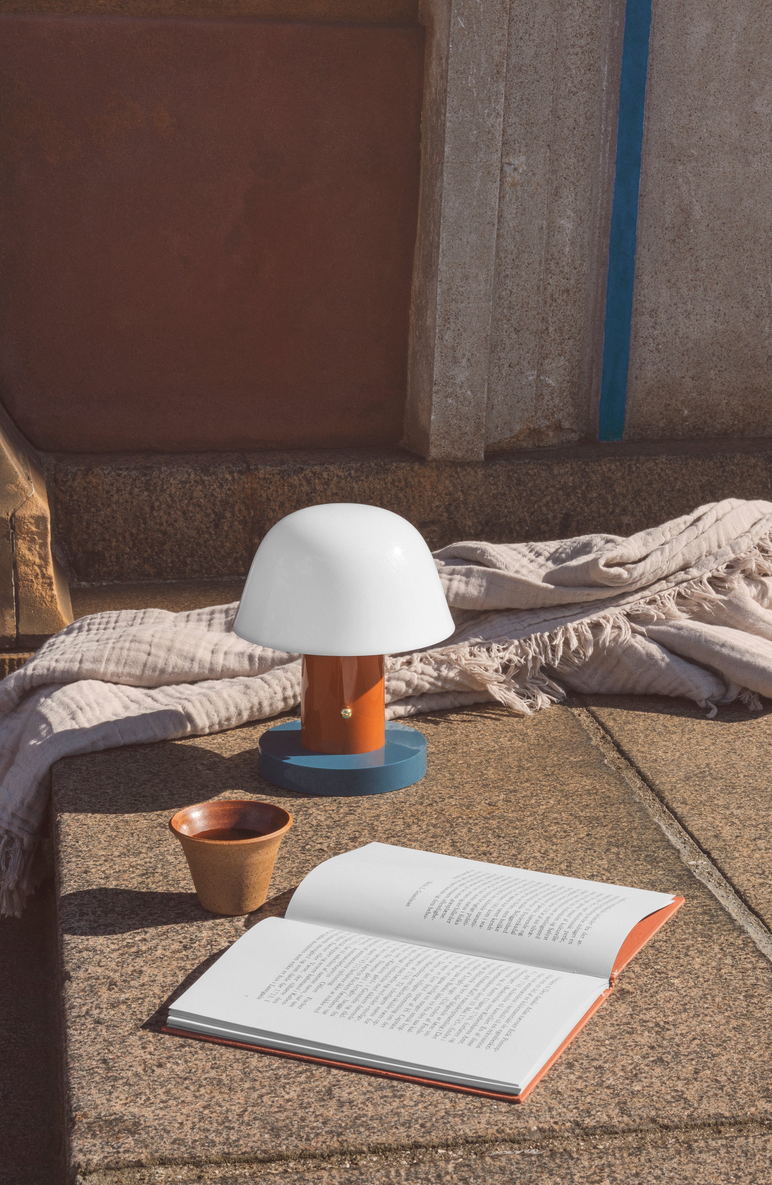 Prenosná lampa SETAGO JH27 s krémovým tienidlo a oranžovo-modrým podstavcom.
