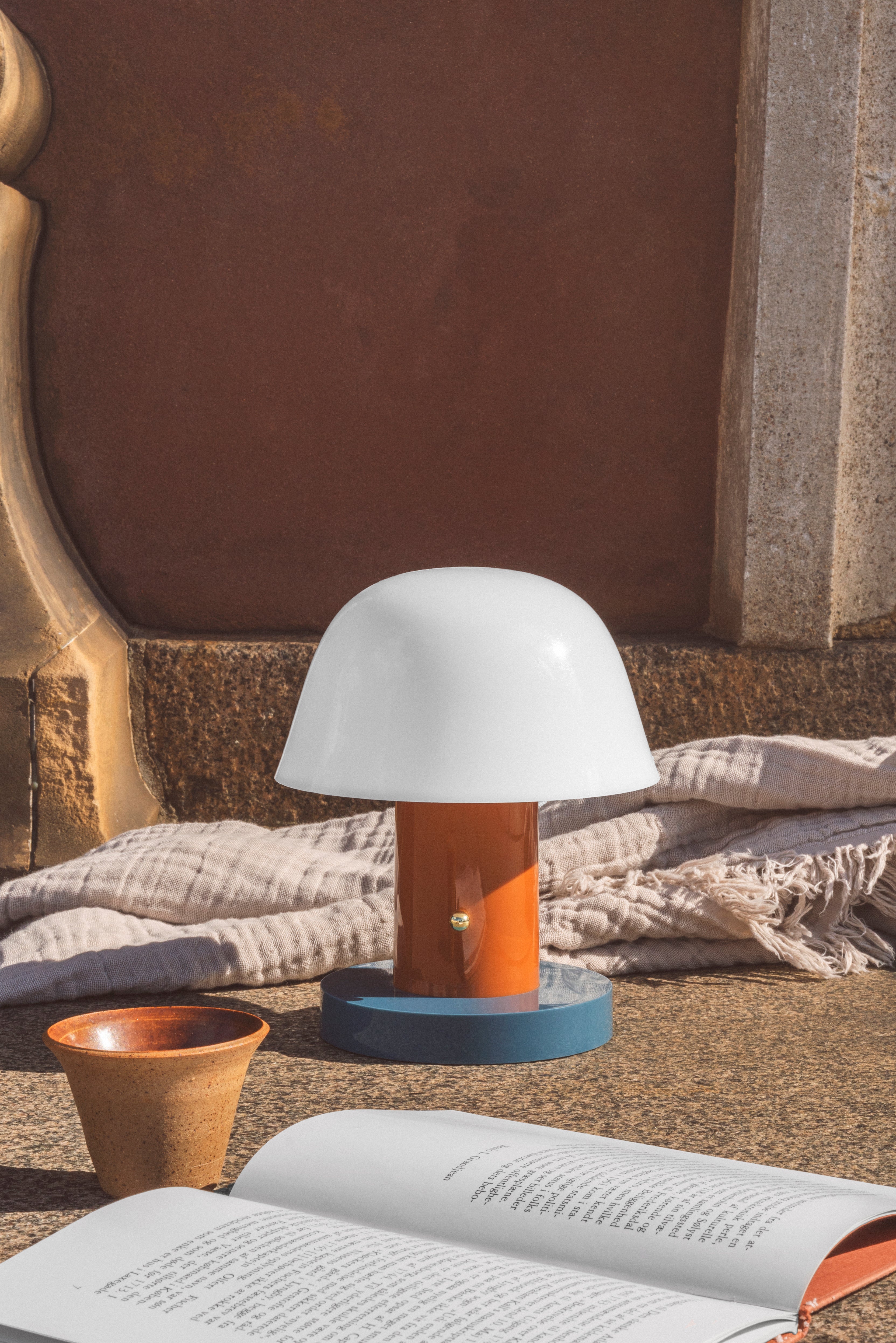 Prenosná lampa SETAGO JH27 s krémovým tienidlo a oranžovo-modrým podstavcom.